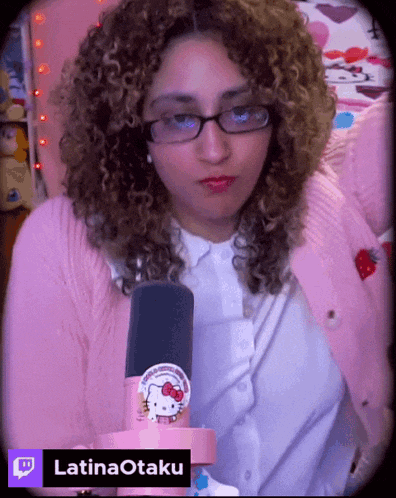 a woman with curly hair is wearing glasses and a pink sweater and has a hello kitty sticker on her shirt