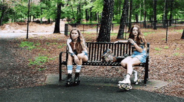 two girls are sitting on a bench in a park with roller skates .