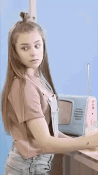 a girl in overalls is standing in front of a pink television