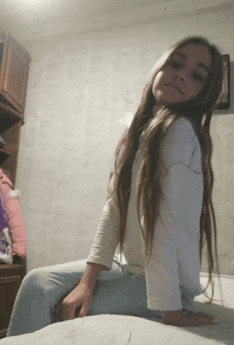 a girl with long hair is sitting on a bed with her hands on her knees