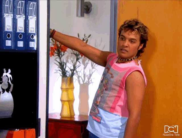 a man in a pink tank top is standing in front of a shelf with binders that say carta on them