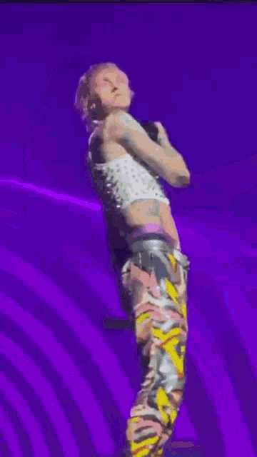 a man with pink hair is standing on a stage with his arms outstretched .