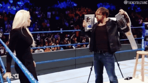 a man in a wrestling ring holds up a trophy and talks to a woman