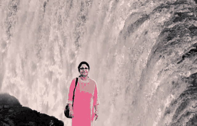 a woman standing in front of a waterfall wearing a pink dress