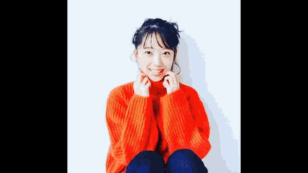 a young woman in a red sweater is sitting on the floor .