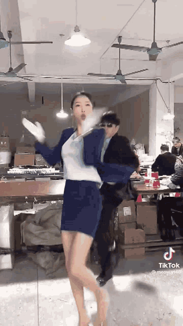 a woman is dancing in a room with a man in a suit behind her .