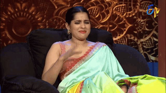 a woman in a saree is sitting on a couch with a tv logo in the background