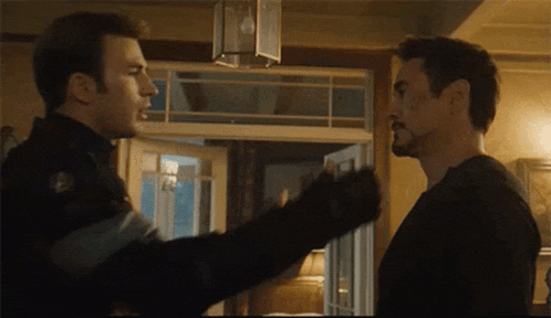 two men are standing next to each other in a room and talking .