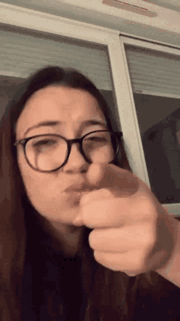 a woman wearing glasses is pointing at the camera with her finger