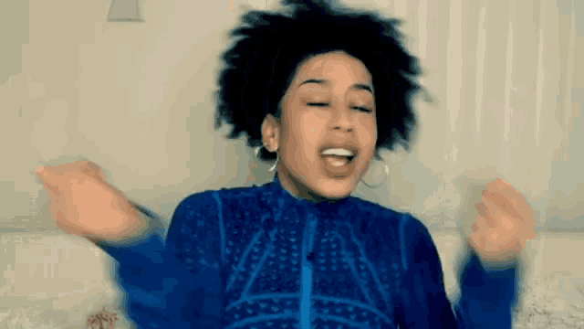 a woman in a blue shirt is making a funny face with her arms outstretched