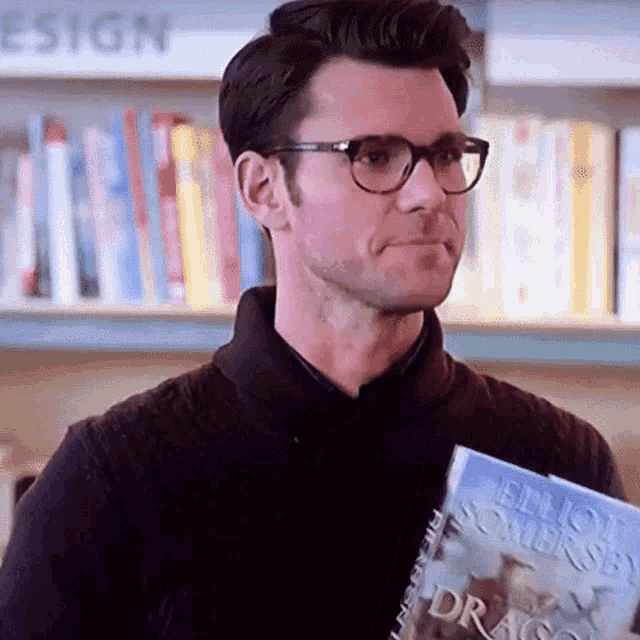 a man wearing glasses is holding a book in his hand in a library .