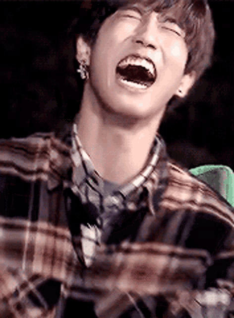 a young man in a plaid shirt is laughing with his mouth wide open .
