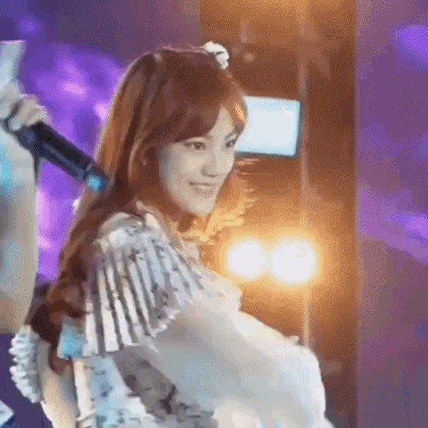 a woman is holding a microphone in her hand and smiling while standing on a stage .
