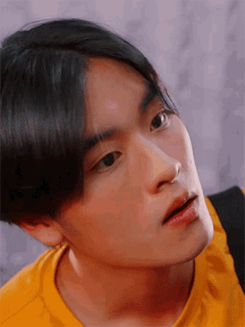 a close up of a young man 's face with a yellow shirt on