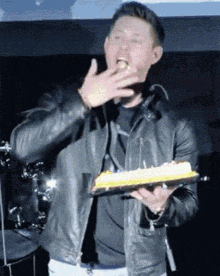a man in a leather jacket is holding a birthday cake and blowing out the candles on it .