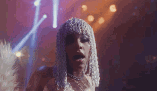 a woman in a silver wig is dancing on a stage in a club .