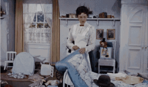 a woman in a white apron is standing in a messy bedroom
