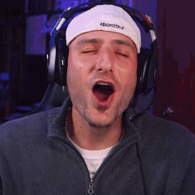 a man wearing headphones and a aeropostale hat is yawning