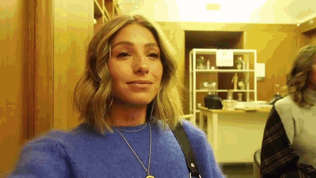 a woman wearing a blue sweater and a necklace is smiling .
