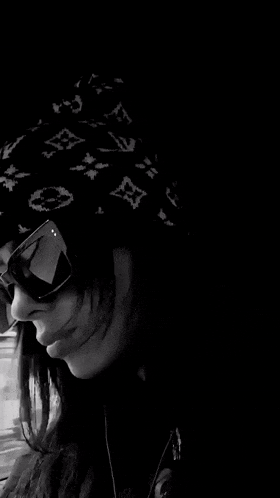 a black and white photo of a person wearing sunglasses and a hat .