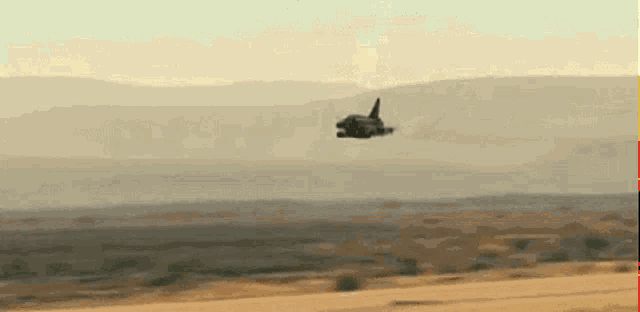 a fighter jet is flying over a desert landscape with mountains in the background .