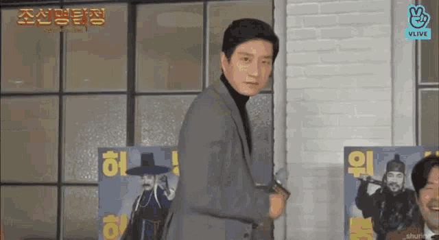 a man in a suit and black turtleneck is standing in front of a brick wall .