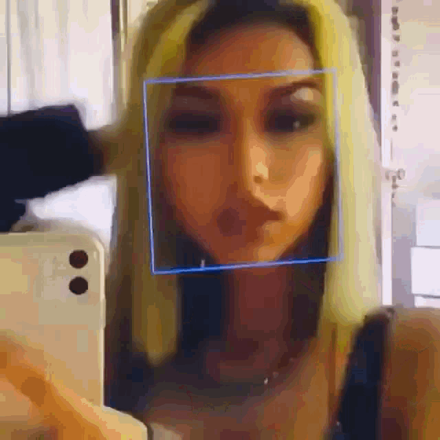 a woman with blonde hair is taking a selfie in front of a cell phone .