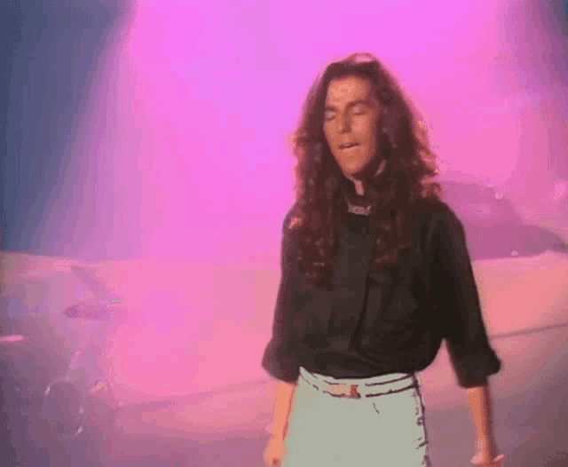 a woman in a black shirt is standing in front of a pink background .