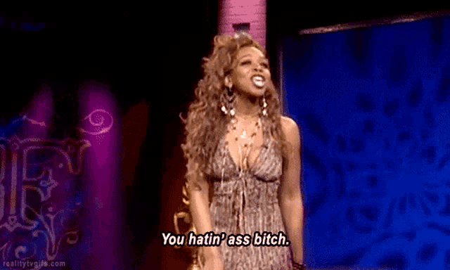 a woman in a dress is standing in front of a blue background and says you hatin ' ass bitch .