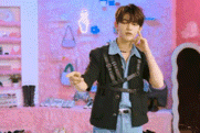 a man in a black jacket is standing in front of a pink wall and a mirror .