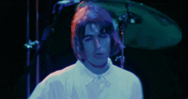 a man in a white shirt stands in front of a drum set in a dark room