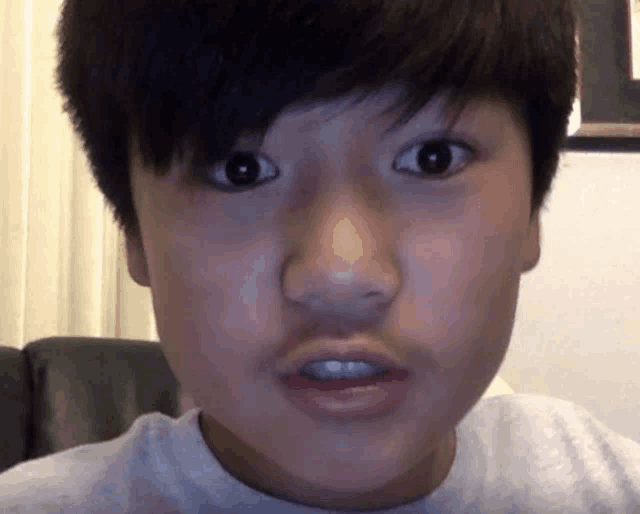 a close up of a young boy 's face with a white shirt on