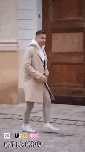 a man wearing a tan coat and a white hoodie walks down a street