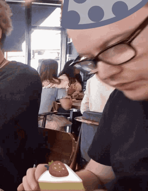 a man with glasses is holding a piece of cake with a strawberry on it