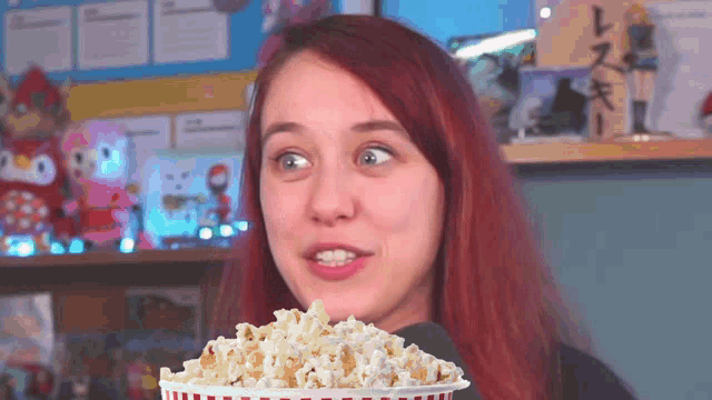 a girl with red hair is holding a bucket of popcorn