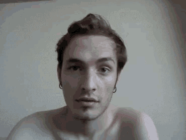 a shirtless young man with a beard and earrings is looking at the camera .