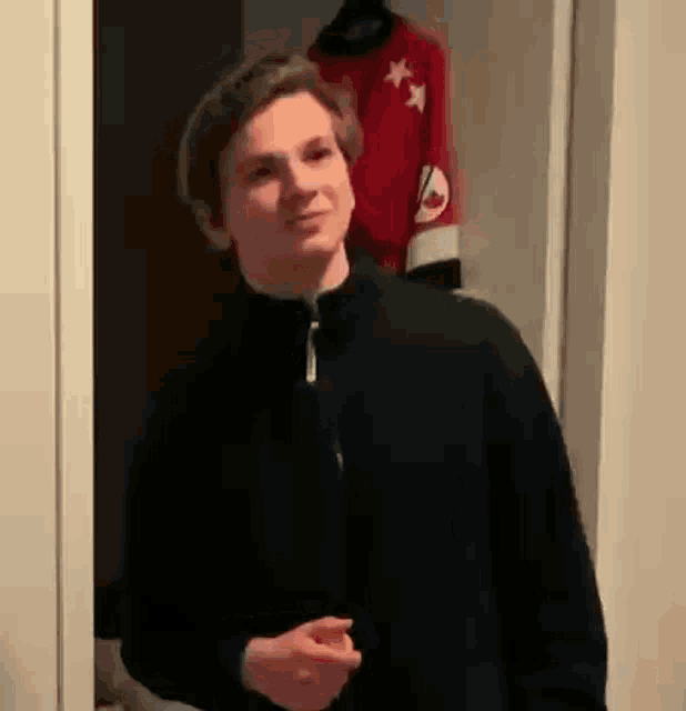 a young man in a black jacket is standing in a doorway in front of a red jersey .