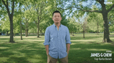 a man in a blue shirt is standing in a park with trees in the background