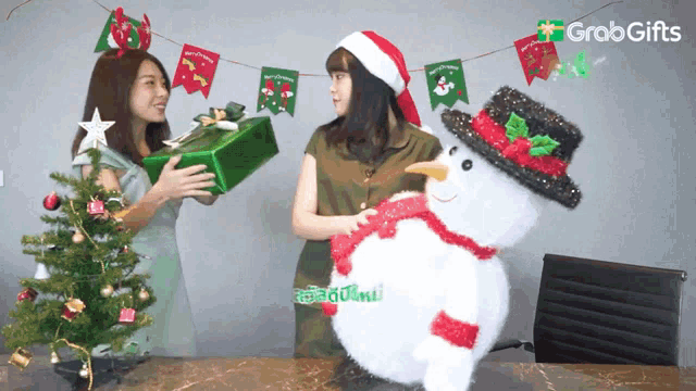 two women standing next to a snowman and a christmas tree with a grab gifts logo in the background