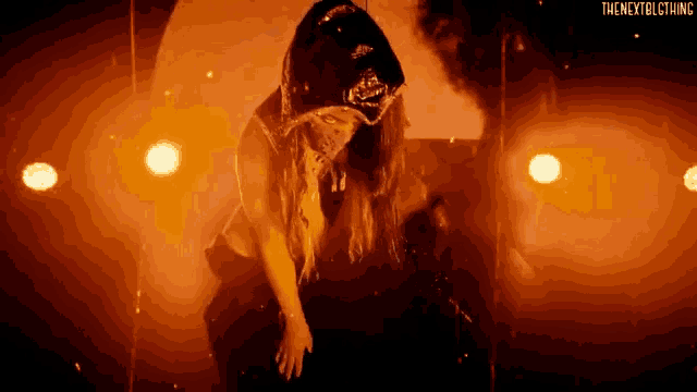 a woman in a hooded jacket is standing in a dark room surrounded by fire .