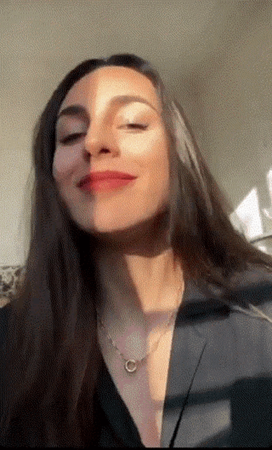 a woman wearing a necklace and a black jacket is smiling