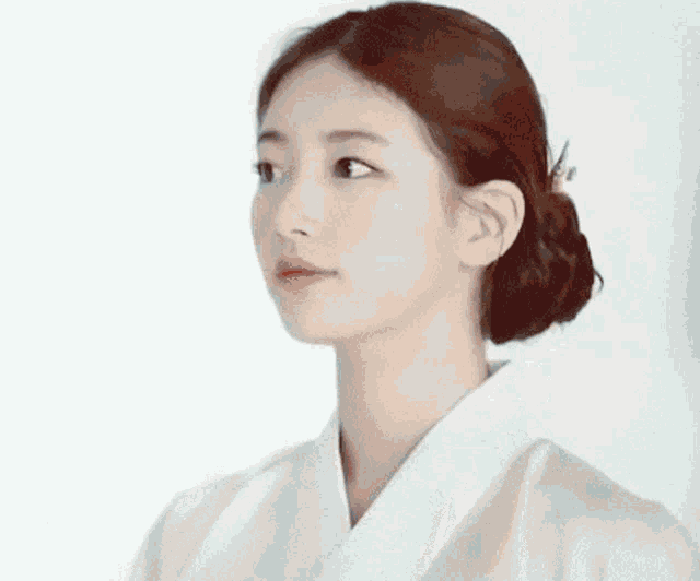 a close up of a woman wearing a white kimono with her hair in a bun