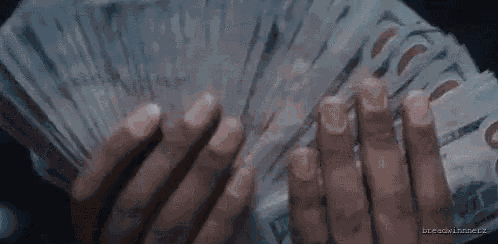 a person is holding a fan of money in their hands in a dark room .