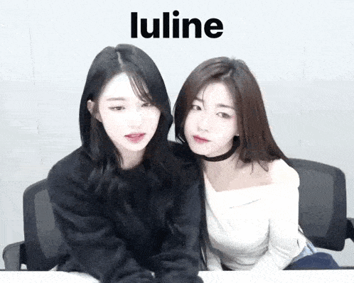 two young women are sitting next to each other at a table and looking at the camera .