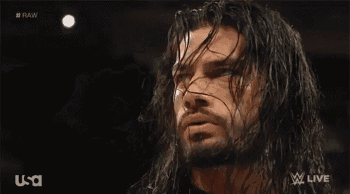 a man with long hair and a beard is holding his hair in his hand while looking at the camera .