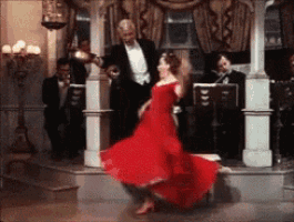 a woman in a red dress is dancing in front of a man in a tuxedo