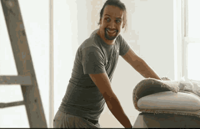 a man in a grey shirt is smiling while holding a rug