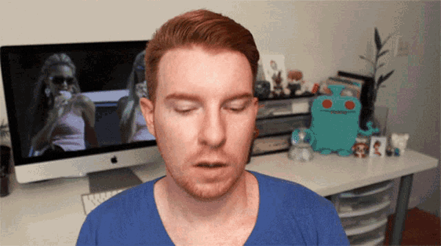a man with his eyes closed is standing in front of an apple computer