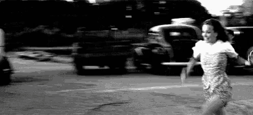 a woman in a dress is running down the street in a black and white photo .