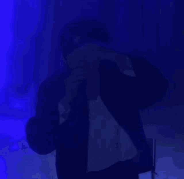 a man is standing in front of a microphone in a dark room with blue lights .